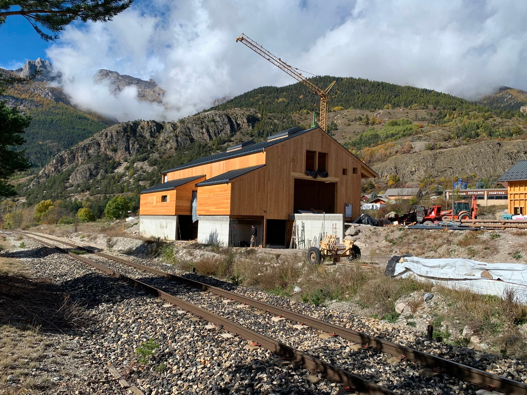 Chalet à ossature bois en construction avec grue de chantier, vue montagne